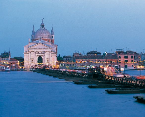 Venezia, festa del redentore La terza domenica di luglio si celebra con grande solennità la festa del Redentore. E’ una tradizione antichissima che risale alla fine della peste del 1576, quando il Senato della Repubblica decretò di innalzare il tempio votivo del Redentore alla Giudecca. Un ponte di barche collega le Fondamenta delle Zattere col tempio palladiano e tutta la città si reca in pellegrinaggio, ma la vera festa, in un tripudio di colori, si verifica la sera della vigilia con lo spettacolo pirotecnico in laguna, a cui assistono tutti i veneziani con le loro imbarcazioni ben addobbate di fronde d’albero e palloncini multicolori.