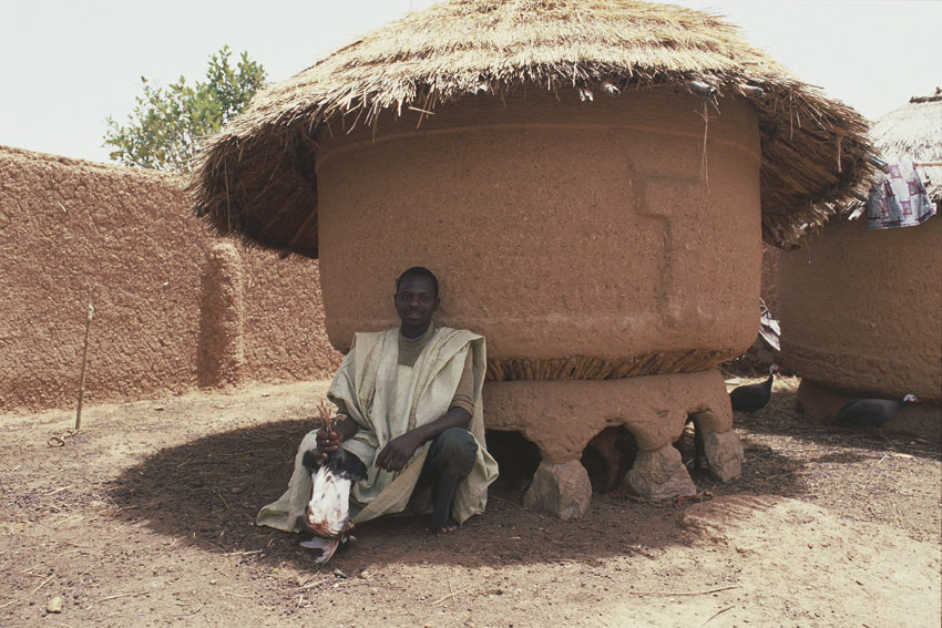 Un uomo di etnia Haussa davanti a un edificio del suo villaggio. Ancora oggi nei territori rurali la popolazione vive per lo più in villaggi, che assumono forme diverse passando dal Nord e dal Centro, dove domina il raggruppamento di capanne circolari, fino al Sud, dove le capanne a pianta rettangolare si allineano lungo le strade.